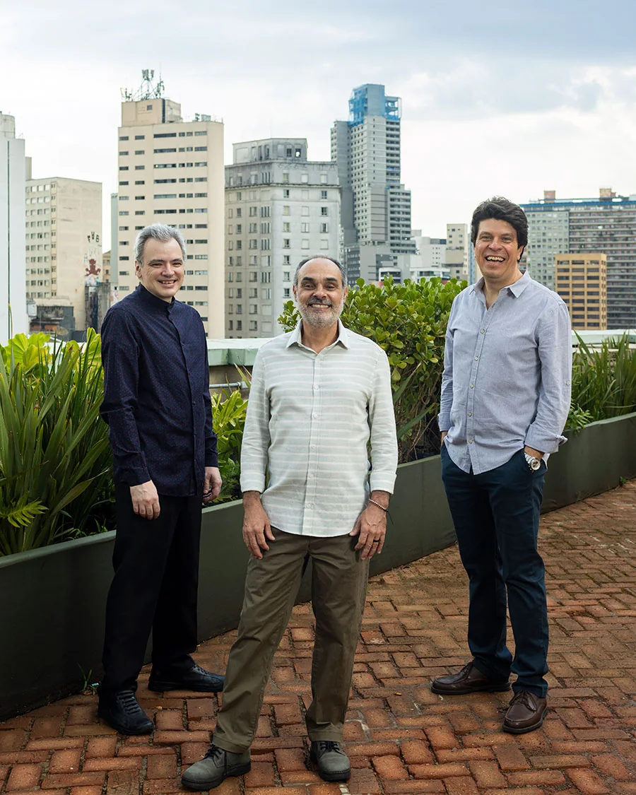 Los tres músicos de Trio Corrente de pie en una terraza de São Paulo, con la ciudad al fondo